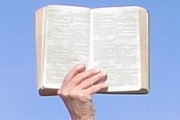 An open Holy Bible held up against a blue sky to indicate the supremacy of the Word of God.