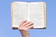 An open Holy Bible held up against a blue sky to indicate the supremacy of the Word of God.